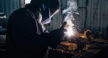 Blacksmith in welding mask welding metal in workshop